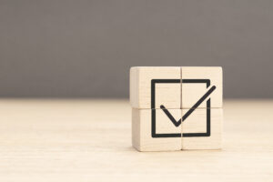 Wooden cube with a check mark icon, symbolizing the reduction of paperwork and simplification of your medical device company through compliance management systems, healthcare communication, integrated healthcare, and medical inventory management.
