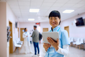 Happy Japanese nurse using touchpad while working in the hospital and looking at camera.