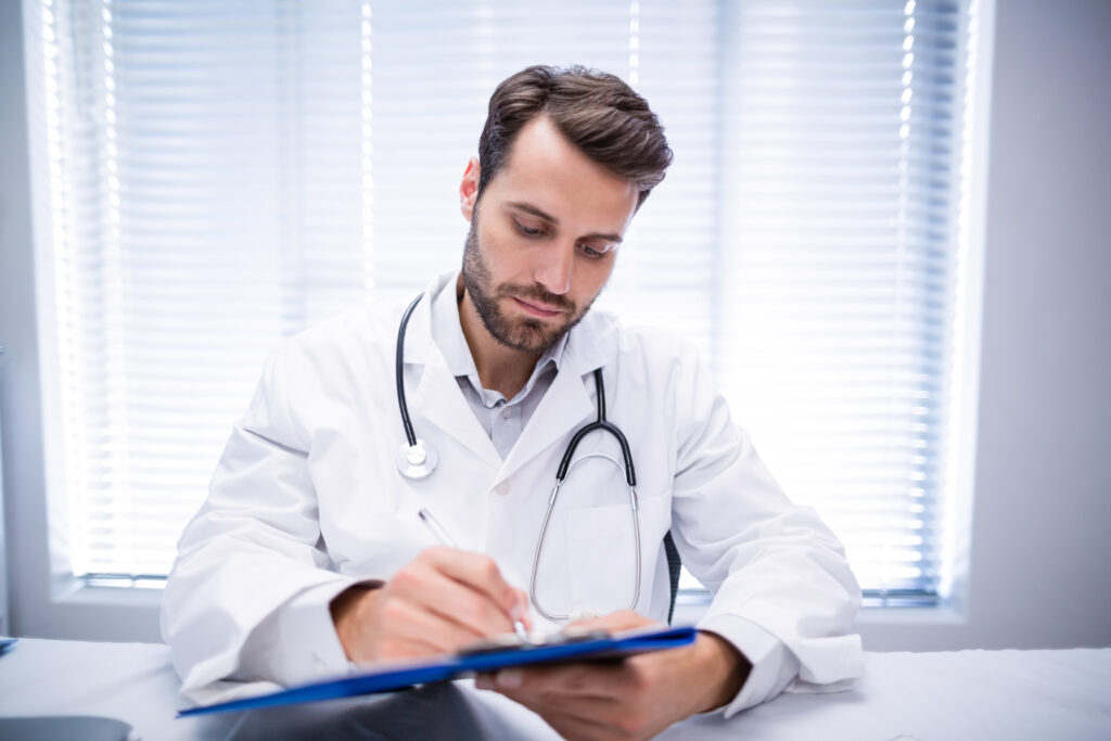 Male doctor writing on clipboard - Medical professional using HUB Healthcare, highlighting integrated healthcare, care coordination, healthcare communication, and patient management software.